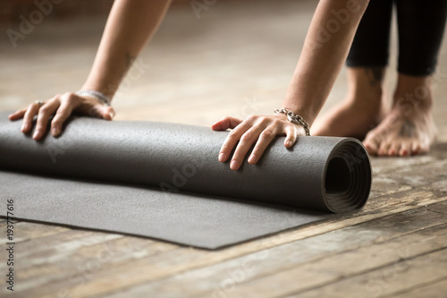 Hands of attractive young woman unfolding black yoga or fitness mat before working out at home in living room or in yoga studio. Healthy habits and lifestyle, weight loss concepts. Close up view photo
