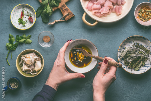 Female hands making marinate for chicken meat meal on kitchen table background with ingredients in bowls , top view. Dieting cooking eating and healthy food concept