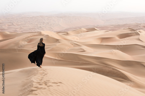Młoda piękna Kaukaska kobieta pozuje w tradycyjnej sukni Emirati - abaya w pustynnym krajobrazie Pustej ćwiartki. Abu Zabi, ZEA.