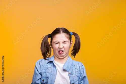 Girl in studio making a disgusted face with eyes closed on yellow background