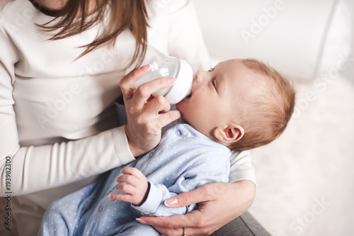 Baby boy drinking milk from bottle holding by mother. Healthy nutrition.