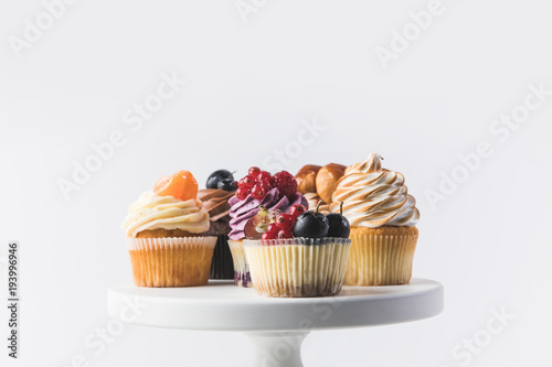 close up view of various sweet cupcakes on cake stand isolated on white