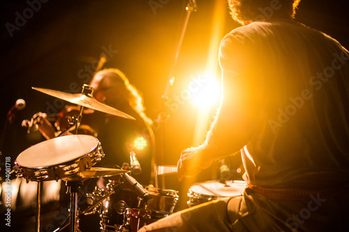 Drummer on stage playing with a band with gold yellow light shining in background 