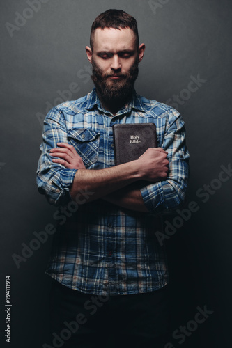 Handsone man reading and praying over Bible in a dark room over gray texture