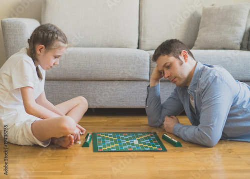 Little girl and her father playing scrabble board game.