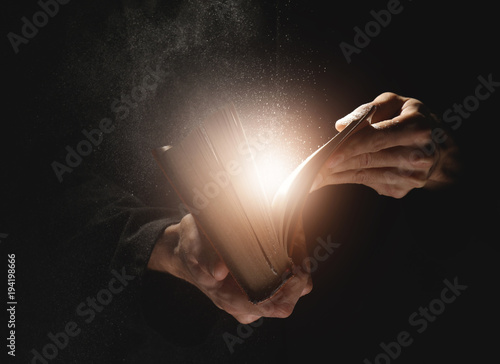 Priest with old Bible on black background, closeup
