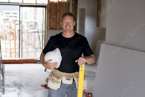 attractive and confident constructor carpenter or builder man with protective helmet posing happy working at industrial construction site