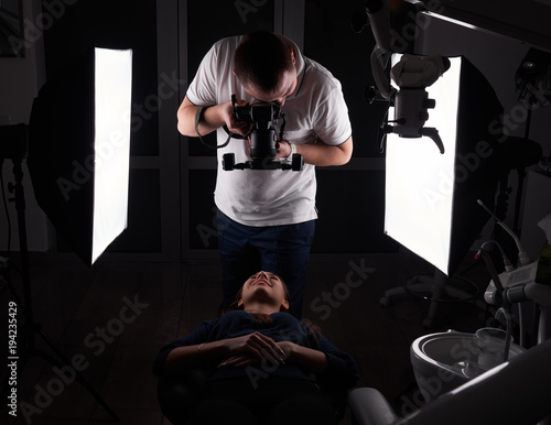 The photographer shoots a model that lies on the dental couch, a photo in the studio, a special light and a camera. Dark studio lighting