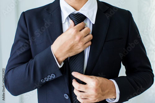 People, business,fashion and clothing concept - close up of man in shirt dressing up and adjusting tie on neck at home.