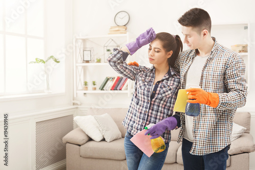 Young couple holding cleaning equipment at home interior background