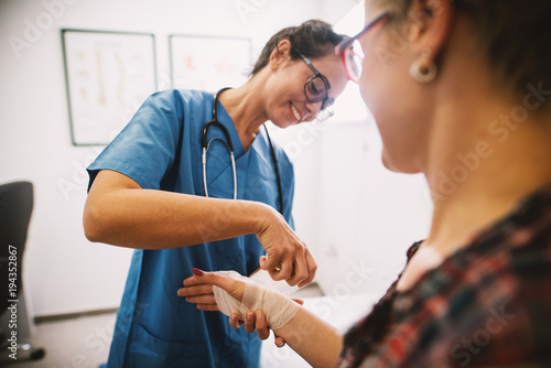 Professional nurse at the hospital bandaging the hand with a medical bandage for a woman patient.