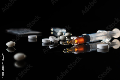 Different drugs - powder and pills and a syringe on a black background. Stop drug addiction. International Day against Drug abuse. Hard drugs on table.