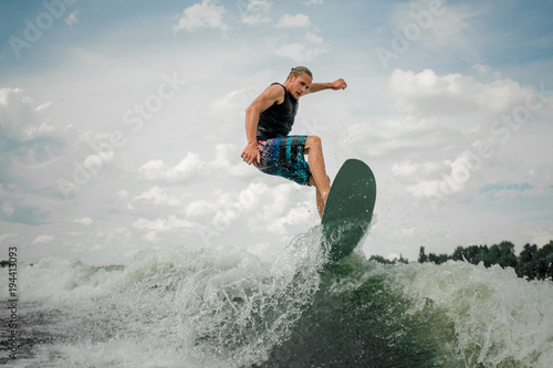 Young and athletic guy wakesurfing on the board down the river