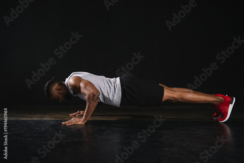 side view of young african american sportsman doing push-ups on black