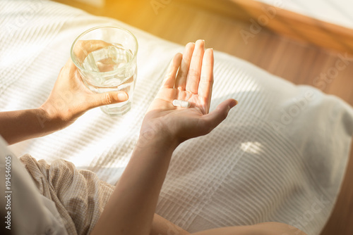 Woman holding pills or capsules on hand and a glass of water