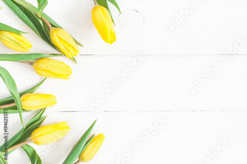 Flowers composition. Frame made of yellow tulip flowers on white wooden background. Flat lay, top view, copy space