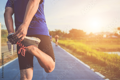 Man workout and wellness concept : Asian runner warm up his body before start running on road in the park. Focus on shoe. Shot in morning time, sunlight and warm effect with copy space 