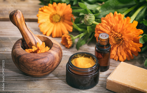 Calendula essential oil, ointment and a mortar on a wooden table, fresh blooming calendula background,