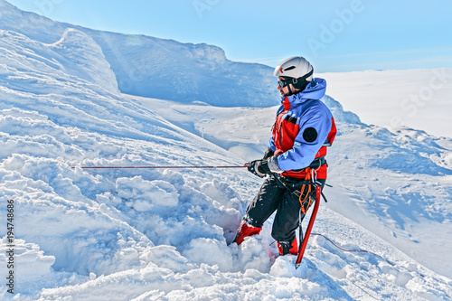 Equipped climber ascent by snowy slope with climbing rope on the top of peak in snowy alpine mountains. Life guard professional man on the work in high mountains. Action in hard conditions scene.