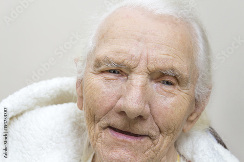 Portret u uśmiechniętej siwej bardzo starej kobiety w szlafroku z kapturem. Twarz bardzo starej siwej kobiety bez zębów.
