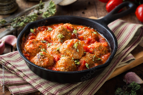 Meatballs in tomato sauce with dried oregano in a rustic vintage cast iron skillet