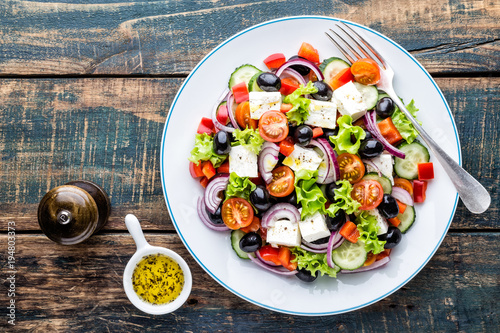 Greek salad of fresh cucumber, tomato, sweet pepper, lettuce, red onion, feta cheese and olives with olive oil. Healthy food, top view