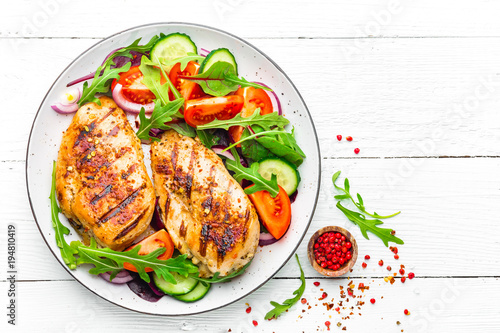 Grilled chicken breast. Fried chicken fillet and fresh vegetable salad of tomatoes, cucumbers and arugula leaves. Chicken meat salad. Healthy food. Flat lay. Top view. White background