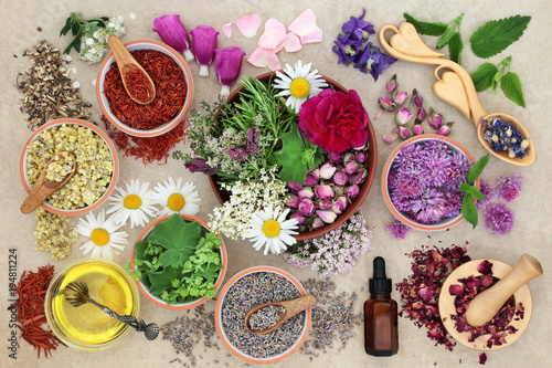 Herbal medicine preparation with herbs and flowers, aromatherapy essential oil bottle and mortar with pestle on hemp paper background. Top view.