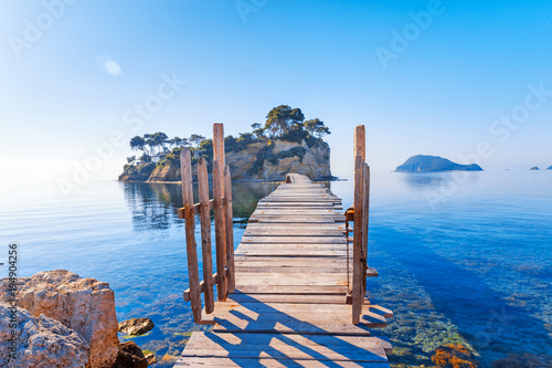 Greece. Picturesque wooden pedestrian Bridge to the small atoll island, view from great Greek Zante or Zakinthos island. Beautiful morning scenery in sunny spring day.