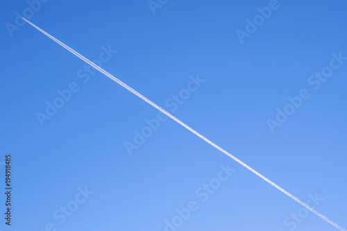 blue background of the sky with a flying plane on it with a white Condensation trail contrail behind it on the entire sky diagonally