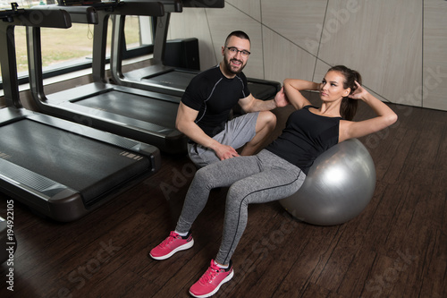 Woman With Personal Trainer On Ball Abs Exercise