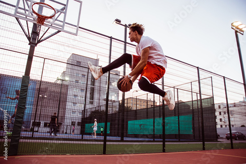 Jump! Full length of young man in sportswear playing basketball on basketball court outdoors