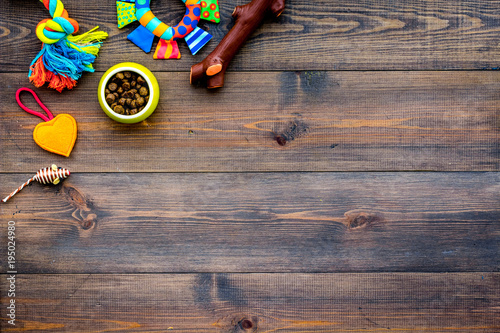 Pet care concept. Toys near bowls with animal feed on dark wooden background top view copy space