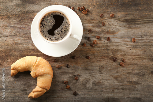 Tasty crescent roll and cup of coffee on wooden background