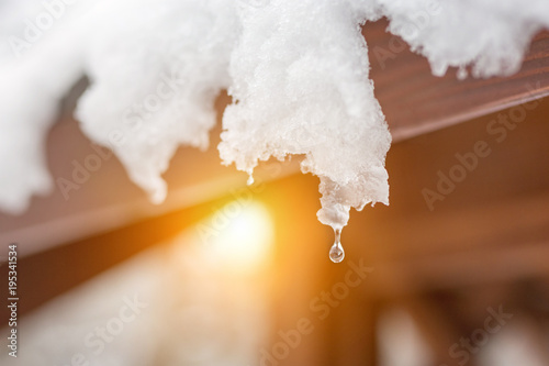 Close-up of melting snow icicles on roof. Falling water drops. Beginning of spring. Meeting cold and heat concept. Fresh spring nature background