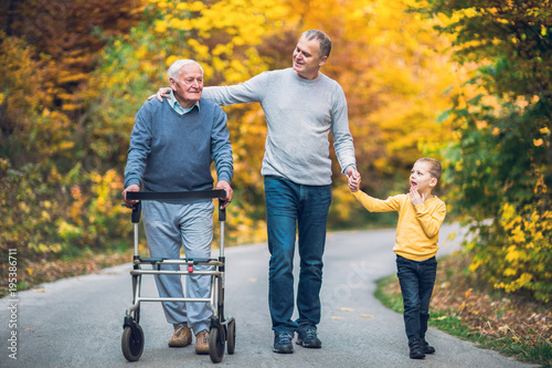 Elderly father adult son and grandson out for a walk in the park.