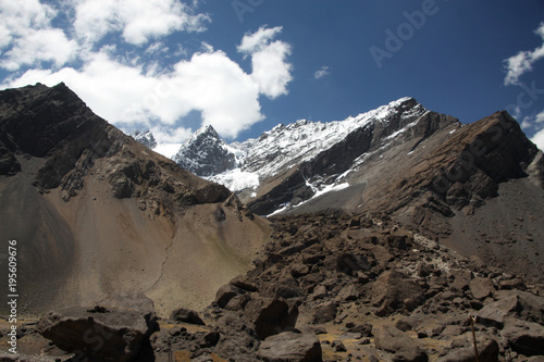 widok na ośnieżone górskie szczyty andów z najwyższym punktem Aconcagua w słoneczny dzień na tle niebieskiego nieba i chmur