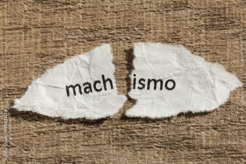 Torn paper written machismo, portuguese and spanish word for chauvism, over wood table. Concept of old and abandoned idea or practice.