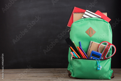 Education concept - school backpack with books and other supplies, blackboard background