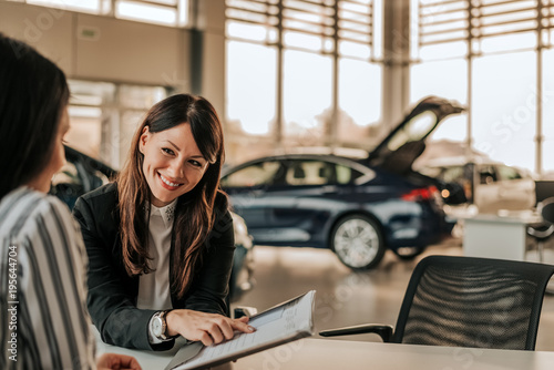 Smiling car saleswoman discussing a contract with a female customer.