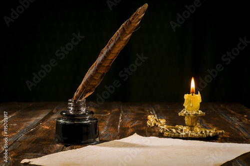 Education and writing concept, pen in ink bottle and candle holder with candle on wooden table.