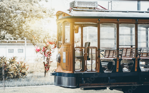 Side shot of empty yellow glossy excursion tram waiting at tramway station: opened interior with wooden windows and seats inside, single headlight, sunny day; Rio de Janeiro, Brazil
