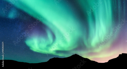 Aurora borealis and silhouette of mountains. Lofoten islands, Norway. Aurora. Green and purple northern lights. Sky with stars and polar lights. Night landscape with aurora, blue sky.Nature background