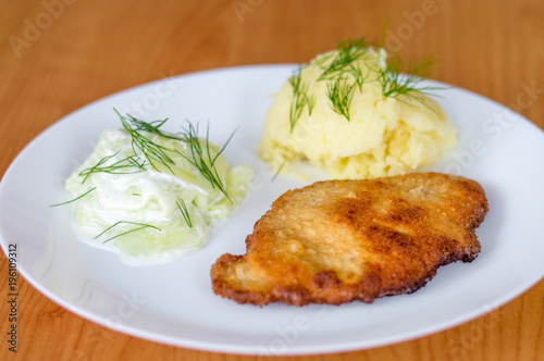 Polish kotlet schabowy (pork chop) with mizeria and mashed potatoes.