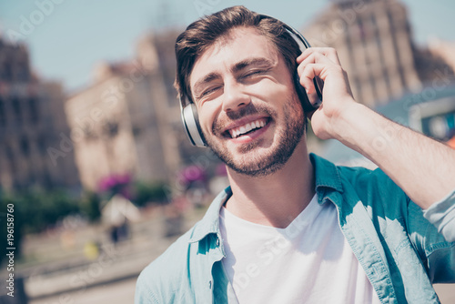 Close up cropped portrait of cheerful laughing delightful excited emotional joyful with stubble toothy beaming smile carefree with modern stylish haircut manager listening to music jeans denim clothes