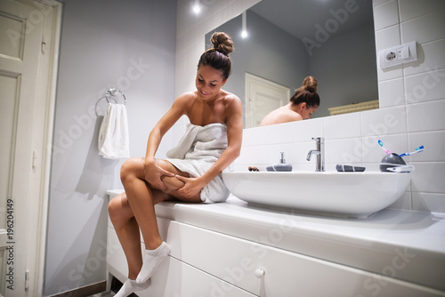 Young cute girl checking cellulite on the leg while sitting on bathroom elements in a towel before showering.