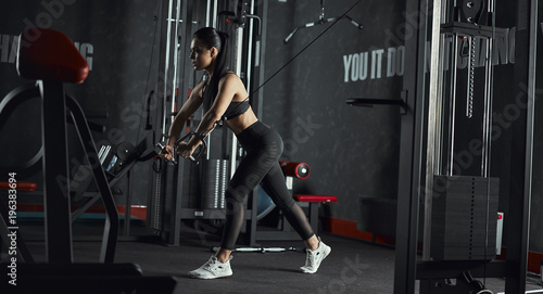 young fitness woman execute exercise with exercise-machine Cable Crossover in gym