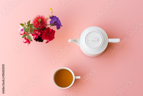 Directly above view of tea with white teapot and colorful flowers on pink background