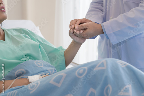 Friendly man doctor hands holding patient hand sitting at the desk for encouragement, empathy, cheering and support while medical examination. Bad news lessening, trust and ethics concept