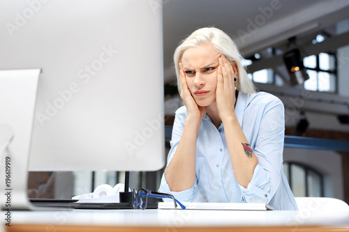 Ból głowy i zmęczenie w pracy. Zmęczona kobieta pracuje przy komputerze. 